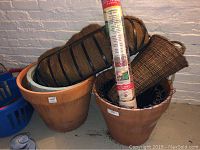 Photo of large terracotta plant containers, wire basket liners, and roll of garden burlap arranged on the floor.