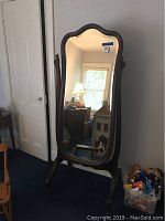 Full view of the wooden freestanding cheval mirror in a room showing the mirror's size, shape, and frame style.