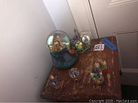 Overview photo of five Disney musical snow globes displayed on a wooden surface against a white wall.