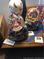 View of two Disney musical snow globes with Winnie the Pooh characters, birthday themes, and resin bases with decorative elements including presents and flowers. Shows slight air bubbles in the glass.