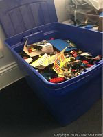 Blue plastic storage bin filled with assorted LEGO bricks and pieces, some paper inserts visible on top.