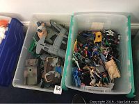 Top-down view of two plastic bins containing mixed action figures and vehicles, including figures from Marvel, DC, Star Wars, Ninja Turtles, and GI Joe along with small vehicles and army men toys.