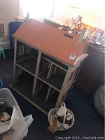 Vintage wooden dollhouse with pink roof and white sides showing wear, placed in a room with other items around.