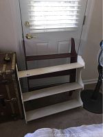 White angled three-tier wooden shelf with brown supports placed inside a room near a door.