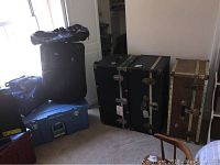 Photo showing all luggage items: three trunks, one suitcase, vinyl totes, and Sterilite box grouped in a room corner