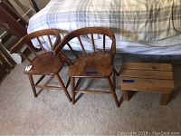 Two vintage wooden child chairs and a wooden foot stool on carpeted floor next to bed