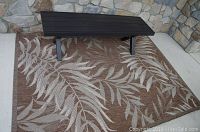 Metal black bench on beige and brown patterned outdoor rug against stone wall
