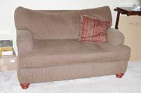 Front view of the brown upholstered Ellis loveseat showing overall condition and style with a patterned red accent pillow on the seat.