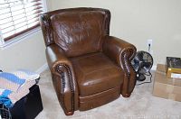 Full front view of brown leather recliner showing nailhead trim on arms and signs of wear on the leather.