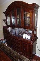 Full frontal view of the large wooden dining room hutch showing upper glass cabinets with glassware and lower cabinet sections with drawers and doors.
