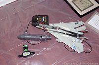 Photo showing Navy fighter jet plane, USS Seawolf submarine, and two remote controls on a pink surface.