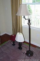 Three lamps set on floor: floor lamp with beige shade, two table lamps with different bases and shades