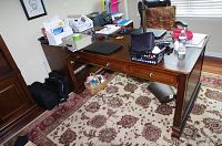 Main wooden desk in a room with drawers partially open, showing wear and clutter on top.