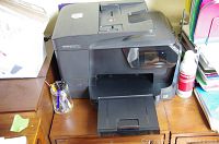 HP OfficeJet Pro 8710 printer on a wooden desk with pens in a glass jar nearby.