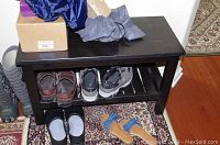 Front view of wooden bench with shoes and boxes on and under it showing overall condition and storage shelf.