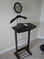Front view of wooden suit stand showing oval mirror, coin tray surface, and hanger.