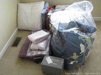 Assorted quilts, comforter and pillows with knee pillow in corner on carpet floor