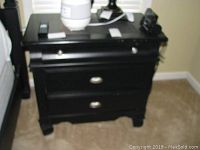 Black wooden night table showing three drawers and surface scratches on top