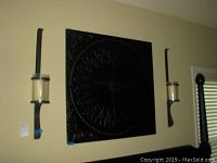 Image showing the metal wall art panel centered between two tall matching candle sconces mounted on a wall.