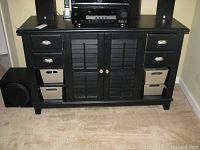 Front view of black wood cabinet showing four drawers, two center doors with slats, and storage bins on shelves.