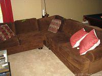 Full view of brown sectional with patterned and red/white throw pillows, showing overall condition and layout.