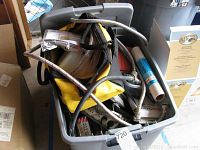 Plastic bin containing assorted hardware parts including metal braided hose, storage bag, flexible tubes, and assorted items