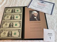 Full view of uncut sheet of four one dollar bills inside a black portfolio with the Official Certificate of Ownership and photo of George Washington on display.