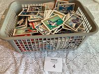 Plastic laundry basket filled with a large collection of mostly baseball cards and some hockey cards, loosely arranged on a table.