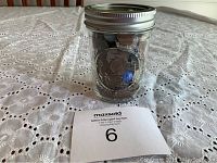 Half pint glass jar filled with coins and a few blue marbles on white crocheted tabletop.