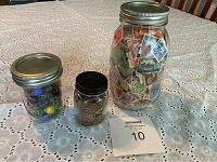Wide view showing three jars on a table: largest jar filled with stamps, medium with marbles, smallest with pennies