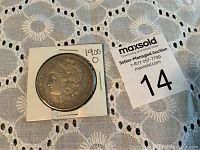 Top view of 1900 O Morgan silver dollar coin in white cardboard holder with handwritten label.