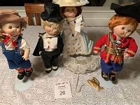 Four Campbell's dolls on stands, posed on a lace tablecloth, showing full group and accessories including a jewelry chain and trophy figurine.