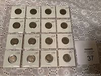 Photo showing 16 nickels laid out on a lace background. 3 Liberty Head nickels and 13 Buffalo nickels housed in white coin holders labeled with years.
