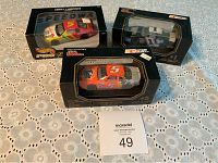 Three NASCAR diecast cars in original boxes displayed on white patterned cloth.