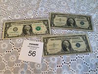 Three U.S. dollar bills displayed on a patterned fabric background, showing front side of the bills with various seals and serial numbers visible.