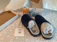 Pair of navy Clarks slippers displayed beside original box on lace tablecloth, stuffed with white paper, showing tops and overall condition.