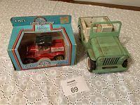 Both items shown side by side on a lace tablecloth: boxed 1918 Ford Runabout die cast metal coin bank in red and a green metal toy Jeep with an open cargo bed.