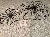 Two rod iron hanging flower wall pieces, one large and one small, placed on a lace tablecloth.