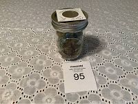 Half pint glass jar with metal lid containing coins and marbles on a white floral-pattern cloth.