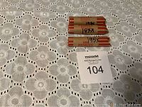 Three rolls of wheat pennies on a white crochet tablecloth, all wrapped in brown paper with printed and handwritten labeling.