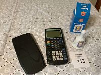 Photo showing Texas Instruments TI 83 Plus calculator, its black cover, Looney Tunes ceramic bell, and the bell's original blue box on a white lace tablecloth.