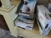 Three boxed appliances shown on a mantle; two Salton portable cooking ranges and one Braun CaféSelect coffee mill