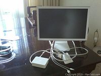 Front view of the Apple LCD monitor on stand with power and video cables on a reflective surface.