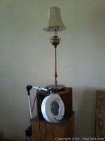 Vintage-style table lamp with gold-colored base and cream fabric shade, alongside a portable magnifying lamp with circular fluorescent light and magnifying glass on an adjustable arm.