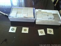 Two white plastic trays filled with cardboard coin flips and four sample flips laid in front