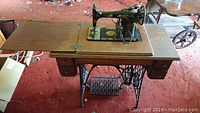 Wide view of the antique Singer sewing machine mounted into the wooden table with drawers and foldable panels.