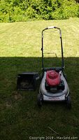 Front view of mower and detached grass collection bag placed on lawn
