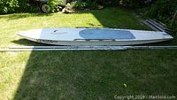Side view of white fiberglass Alcort Sailfish sailboat hull with registration number 50E90205, lying on grass next to spars and rigging.