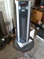 DeLonghi Salem column heater standing on a small round wooden table in a room with fireplace and other items.