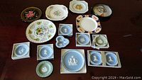 Top-down image showing assortment of Wedgwood Jasperware plates in blue and green hues with white cameos, alongside various decorative floral plates.
